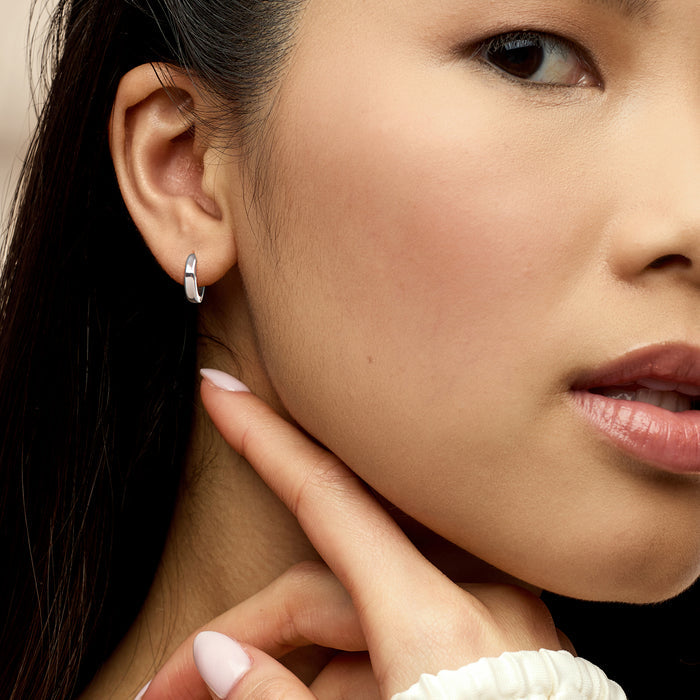 White gold huggie hoop earrings on ear, slender hinged hoop with small clasp