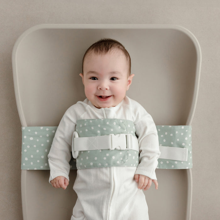 Smiling baby on a change mat wrapped in a Sage Whimsy WriggleBum nappy change harness.
