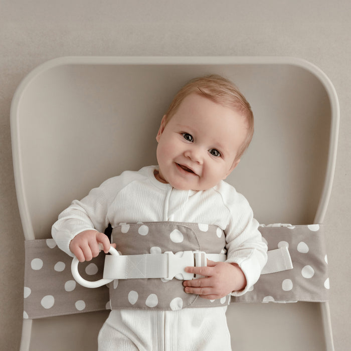 Smiling baby lying on a change mat, with a Spotty Dotty WriggleBum nappy change harness wrapped around them.